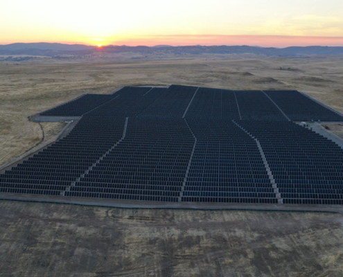 Aerial view of a solar farm in San Joaquin County with the sun setting behind mountains in the distance