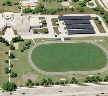 Aerial view of John Paiul II Catholic Secondary School in Ontario, Canada with rendered solar car ports and battery storage systems