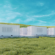 Daytime exterior view of battery energy storage system enclosures in a field under a blue sky