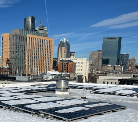 Winter daytime exterior of solar panels on the roof of a building at Northeastern University and a portion of the Boston skyline